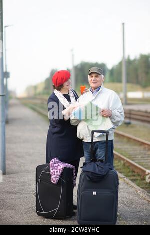 happy senior couple with suitcases looking at the map and waiting for the train to go on a trip Stock Photo