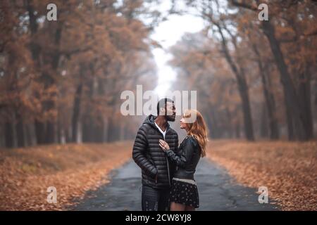 Interracial couple posing in autumn park road, black man and white redhead woman Stock Photo