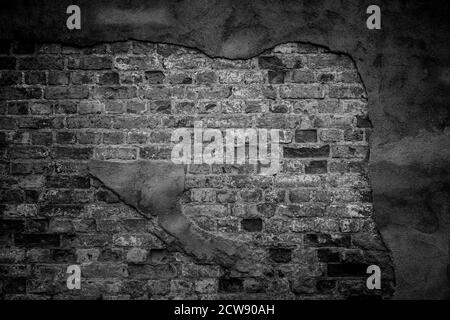 Old, dirty and weathered wall in black&white. Plastering is broken revealing old bricks. Front view. Dark full frame textured background. Stock Photo