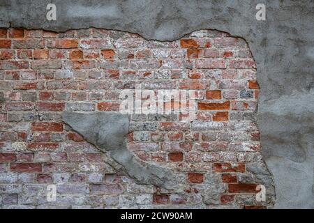 Front view of an old, dirty and weathered wall. Gray plastering is broken revealing old bricks. High resolution full frame textured background.