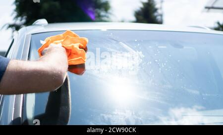 Hand wiping the windshield of a car on a sunny day. Wipe dry with an orange  sponge. Rag wipes water stains on the window Stock Photo - Alamy