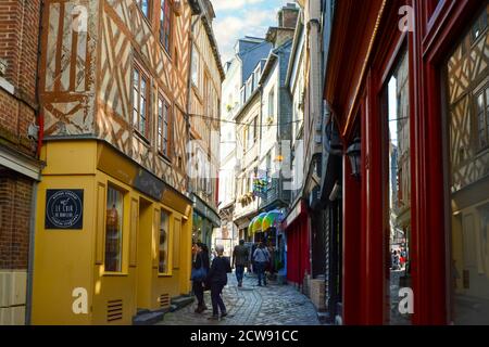 Tourists walk a picturesque back street past half timbered construction shops in the medieval coastal fishing village of Honfleur, in Normandy France Stock Photo