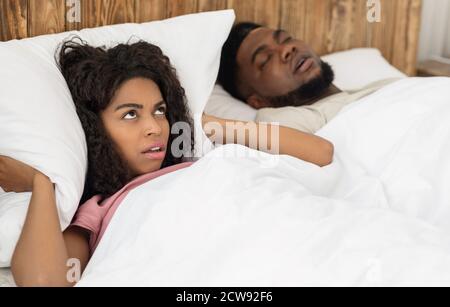 Angry african american woman covering her ears with pillow Stock Photo