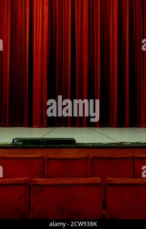 Red theater seats look at a red closed curtain waiting for the performance to start Stock Photo