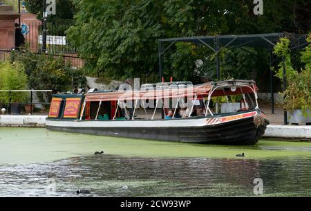 People enjoy a hire boat by Jason's Trip. Picturesque narrow boats at Little Venice in London, England. Pretty house boats are moored on the canals ne Stock Photo