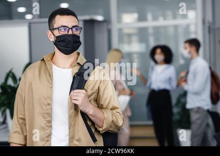 Pandemic and office work with people concept. Focus on millennial man in protective mask and glasses with backpack looking to the side Stock Photo