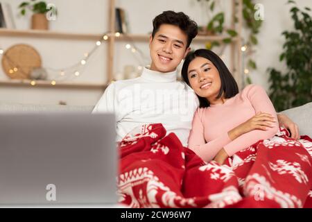 Asian Couple Watching Christmas Movies On Laptop Online At Home Stock Photo