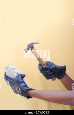 Man's hand holding hammer with stone isolated on yellow backgrounds Stock Photo