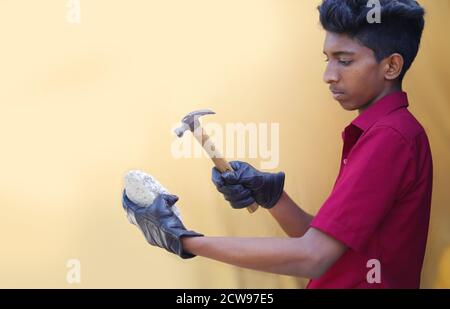 Young mechanics hand holding hammer with stone isolated on yellow backgrounds Stock Photo