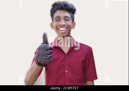 Smiling young mechanic in uniform with showing thumbs up in gray backgrounds Stock Photo