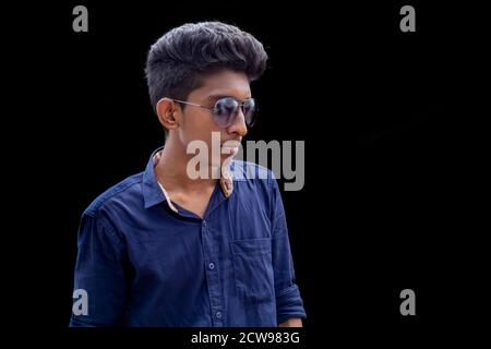 Handsome fashion man hipster in stylish sunglasses in a blue shirt posing near a black backgrounds Stock Photo