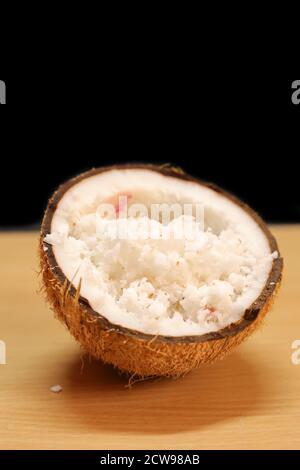 Coconuts with coconut flakes are isolated on a wooden table on a black backgrounds Stock Photo