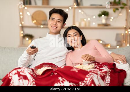 Asian Couple Watching Christmas Movies On TV Sitting At Home Stock Photo