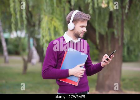 unshaven guy holding notebook and listening music in earphones from smartphone, education. Stock Photo