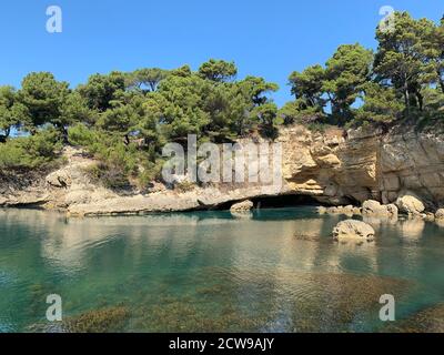 Scenic rocky Mediterranean beach. Turquoise calm water of Adriatic sea. Pine trees on the cliff. Sea cave. Coastal rocks.Summer vacation in Montenegro