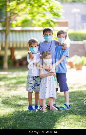 Young children in protective masks on faces outdoors. Quarantine. Kids wearing safety masks while posing in summer park. Coronavirus prevention. Stock Photo