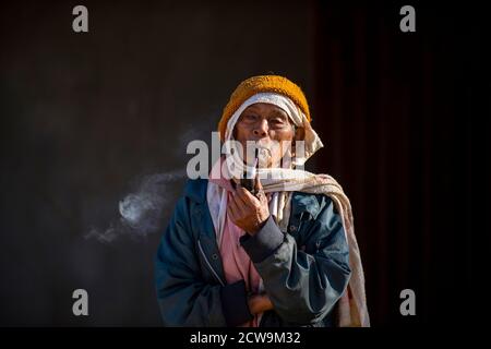 Chiang Mai / Thailand - Jan 16 2016 : Old Asian man carrying a pipe and smoking, wearing old clothes and a turban. Black background, hill tribe men in Stock Photo