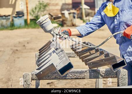 Unrecognizable male worker in protective costume and gloves using spray gun and painting metal stair stringer Stock Photo