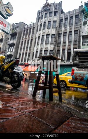 A wooden stool sits in the pouring rain at the curb of a busy street with no owner in sight in Bangkok's Chinatown. Stock Photo