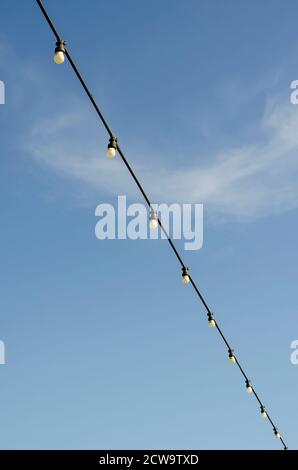 Garland with light bulbs on a background of blue sky. One wire diagonally. Minimalism. Festive concept. Stock Photo