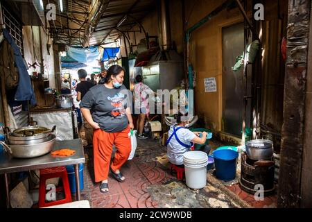 A large woman walks through a restaurant and looks at employee washing pots, pans and dishes. Stock Photo