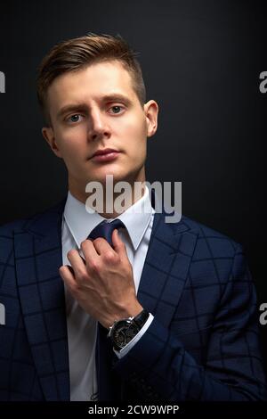 serious confident guy in executive suit fix a tie isolated over black background. trendy rich guy posing at camera Stock Photo