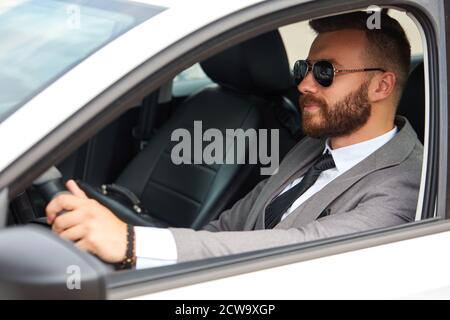 cool businessman in black sunglasses sits inside of car, drive it. successful male in formalwear, in suit. Stock Photo