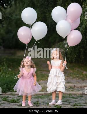 Little girls in pink and white dressses with balloons walking in the park Stock Photo