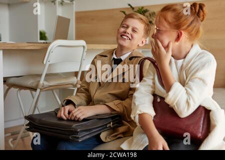 positive caucasian children girl and boy sit together on bed in hotel or at home, waiting for departure or leaving, smie, have fun Stock Photo