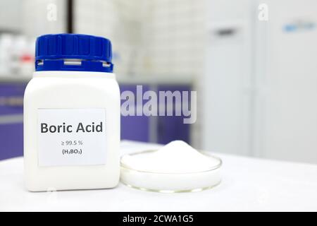 Selective focus of a bottle of pure boric acid chemical compound beside a petri dish with solid crystalline powder substance. White Chemistry laborato Stock Photo