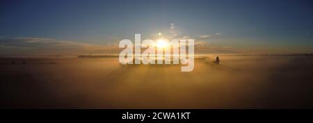 Morning fog and sunlight illuminating the cream of the trees. Panoramic shot of rural nature, view from the drone. Stock Photo