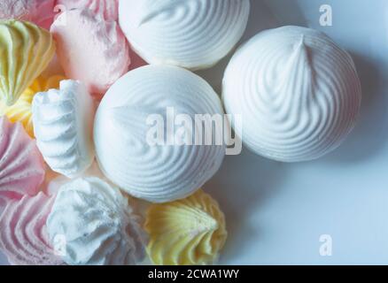 Top view of pink, white and yellow meringues and white marshmallows on a white background close up Stock Photo
