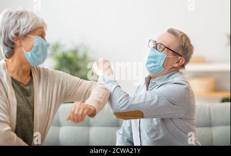 Senior couple wearing face masks and greeting bumping elbows during coronavirus and flu outbreak. Virus and illness protection, home quarantine. COVID Stock Photo