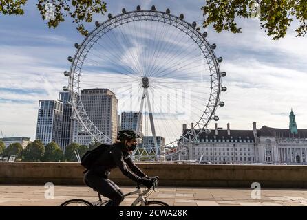 London, Britain. 28th Sep, 2020. A woman wearing a face mask cycles past the London Eye in London, Britain, on Sept. 28, 2020. Global COVID-19 deaths reached the grim milestone of 1 million on Monday, according to the Center for Systems Science and Engineering (CSSE) at Johns Hopkins University. Credit: Han Yan/Xinhua/Alamy Live News Stock Photo