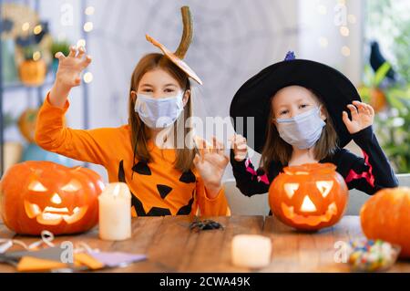 Cute little children girls in carnival costumes wearing face masks. Happy family preparing for Halloween protecting from COVID-19. Stock Photo