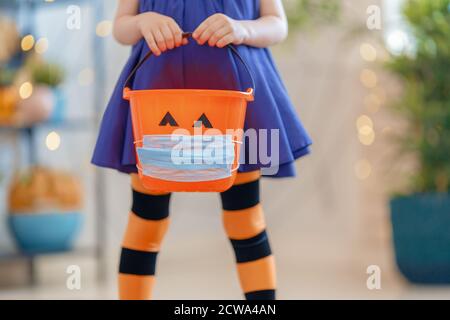 Happy Halloween! Little kid with a basket for sweets  wearing face mask protecting from COVID-19. Stock Photo