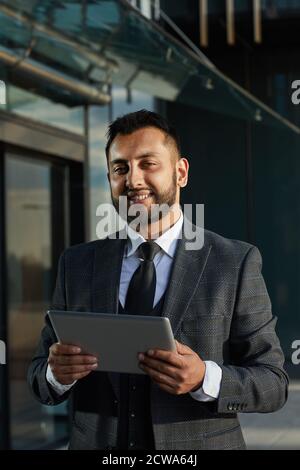Portrait of bearded businessman in elegant suit smiling at camera while using tablet pc outdoors Stock Photo