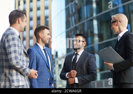 Young bearded businessman talking to his colleagues and smiling while they standing in the city Stock Photo