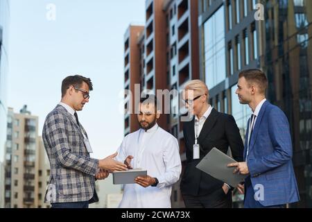 Businessman using digital tablet and discussing online presentation with his colleagues while they standing in the city outdoors Stock Photo