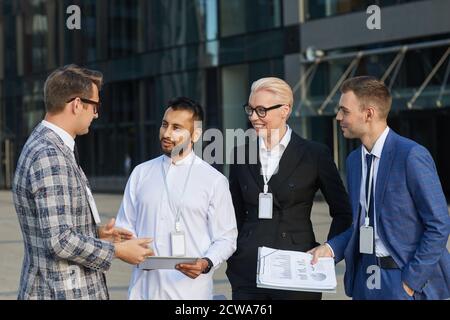 Members of business conference discussing online presentation using digital tablet standing outdoors in the city Stock Photo