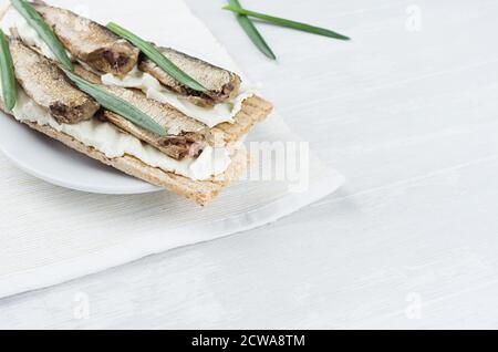 Fresh spring vitamine sandwiches of flat cereal wheat dry crisps bread with cream cheese, fish preserves, green onion on white wooden table, closeup, Stock Photo