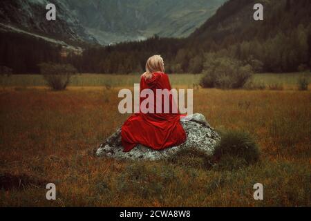 Blond woman with red cloak. Alone on a rock Stock Photo