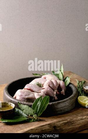 Raw uncooked quails ready for marinat in clay tray with lime, salt, pepper and greens over wooden cutting board. Stock Photo
