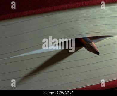Pencil used as bookmark in a closed thick book casting shadow on its pages. Concept : reading, studying, acquiring knowledge. Stock Photo