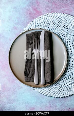 Empty ceramic plate with fork and knife on textile napkin on knitted round napkin over blue concrete background. Flat lay, space Stock Photo