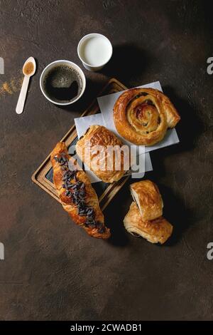 Variety of traditional french puff pastry buns with rasin and chocolate, croissant with paper cup of coffee and milk, recycled wooden spoon of cane su Stock Photo