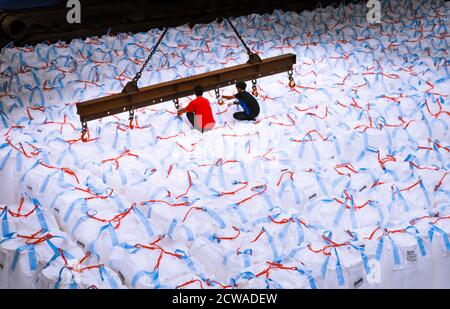 Overhead crane lift jumbo bags of tapioca using spread bar in storage warehouse. Bulk cargo in jumbo bag handling equipment. Stock Photo