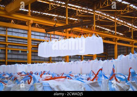 Overhead crane lift jumbo bags of tapioca using spread bar in storage warehouse. Bulk cargo in jumbo bag handling equipment. Stock Photo