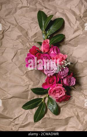 Creative layout with beautiful pink roses flowers and green leaves on crumpled craft paper background. Flat lay. Greeting card concept Stock Photo