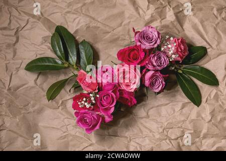Creative layout with beautiful pink roses flowers and green leaves on crumpled craft paper background. Flat lay. Greeting card concept Stock Photo